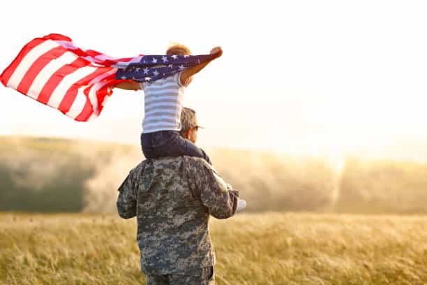 Rear view of military man father carrying happy little son with american flag on shoulders and enjoying amazing summer nature view on sunny day, happy male soldier dad reunited with son after US army